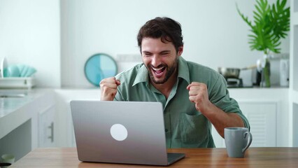 Successful young dark-haired Caucasian businessman in casual wear, rejoicing and clenching fists from excitement while working on laptop from home. Goal achievement. Successful deal. Online business