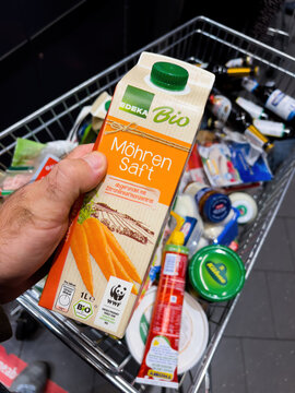 Frankfurt, Germany - Sep 17, 2022: POV male hand with Mohren Saft carrots juice pack bio organic by Edeka above a full shopping cart of groceries at a convenience store