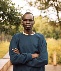 Portrait of a young african man who stands with his arms crossed on a summer day in the park