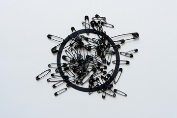 pile of black safety pins and black paper ring on blank paper