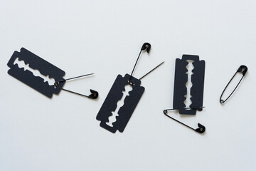 paper silhouette of razor blades (glyph or dingbat) and open safety pins on blank paper