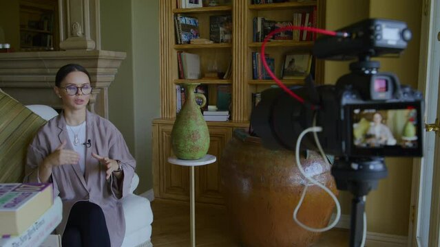 Close-up view of a woman in smart outfit and glasses in antique interior. Caucasian, adult lady in her 30s gives interview with a lavalier microphone on her clothes. Video recording. High quality 4k