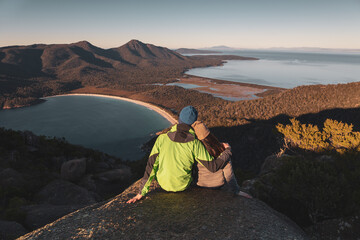 A pair of traveller couple watching sunrise at the peak of Mount Amos with Wineglass Bay at the...