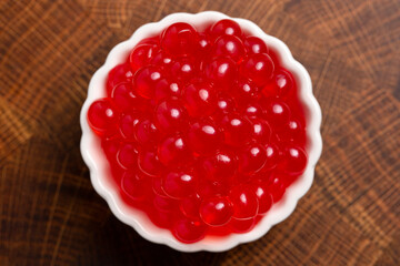 A Bowl Filled with Red Popping Boba on a Wood Background