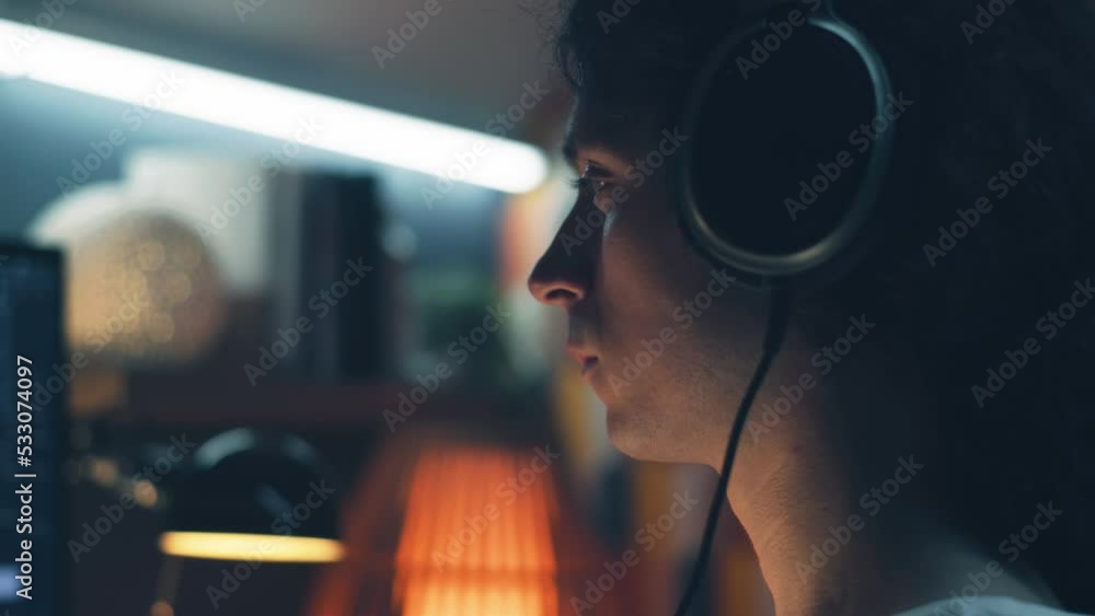 Poster man in headphones browsing the internet and social networks on computer at home at night and listeni