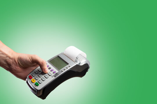 A person's hand holds a cash terminal on a green background. Purchases, sales, online trading, credit and bank cards, contactless payments, new financial technologies.