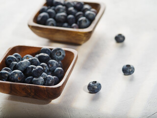 On a white background, two wooden bowls with blueberries. Delicious healthy berries, a lot of vitamins, antioxidants. A ready-to-eat product, an ingredient for many dishes.