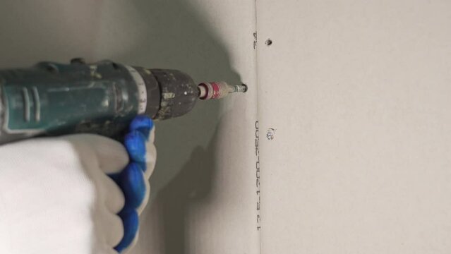 A worker with an accumulator screwdriver to tighten screws into a drywall panel, close-up