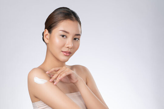Gorgeous girl with soft makeup applying moisturizing skincare cream on shoulder isolated over white background. Skincare cream applied by female model concept.