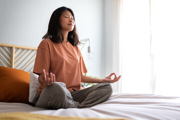 Young asian woman wearing comfortable clothes meditating on the bed in the morning to clear mind....