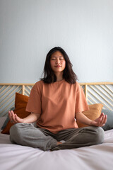 Front view of college student woman meditating and doing breathing exercises on bed in the morning....