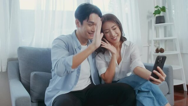Young smiling asian couple holding smartphone and making video call at home