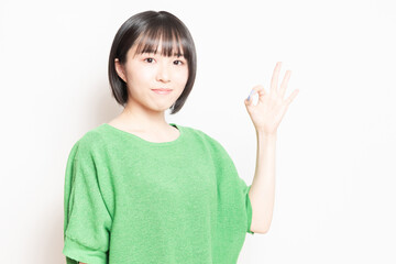 白背景の前でOKのポーズをする若い女性
