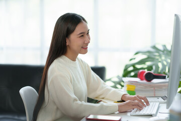 Bright and charming  young Asian woman working on her laptop with the intention of producing a satisfying result.