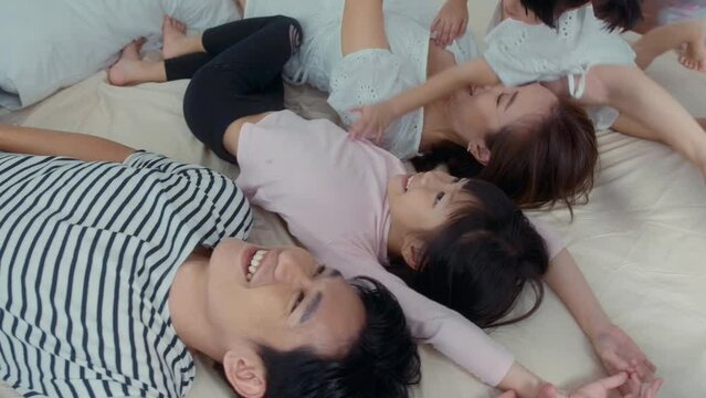 Asian Parents with two little daughters playing, jumping on the bed in bedroom, happy family concept