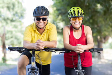 Confident senior couple cyclists leaning on handlebar of bicycle outdoors
