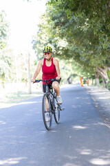 Happy old woman in sportswear riding bicycle outdoors on countryside road

