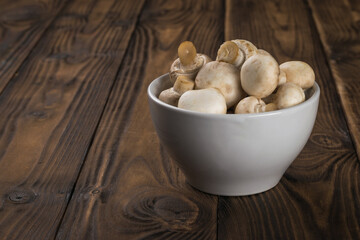 Small mushrooms in a white cup on a wooden table.
