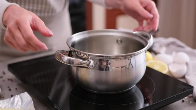 Woman putting pot on induction hob at domestic kitchen