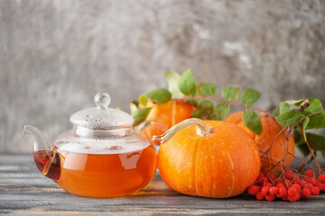 Autumn hot tea in a glass teapot and pumpkins and mountain ash berries. Thanksgiving concept