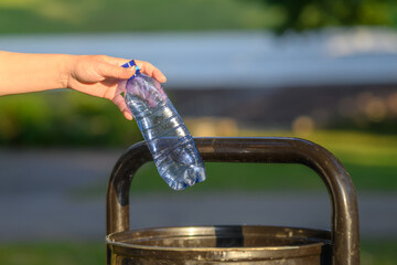 Fototapeta premium A woman throws plastic bottles into a trash can in a city park.