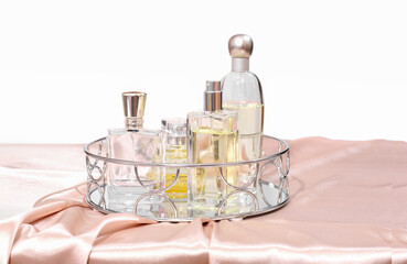 various bottles of perfume on a trendy mirror tray. pink silk satin fabric background. female...