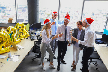 Business people are celebrating holiday in modern office drinking champagne and having fun in coworking. Merry Christmas and Happy New Year 2023.