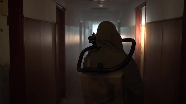 Back view of a survivor of the apocalypse in a gas mask walking with a flashlight through a dark building. Radiation pollution, toxic environment.