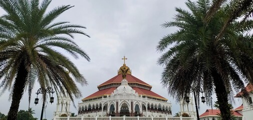 Famous and largest asian christian religion catholic church, chapel, cathedral, forane or shrine beautiful pilgrimage architecture building exterior in kerala india with palm trees and sky background.