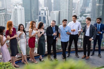 Photo of a group of businessmen and businesswomen mingle with each other drinking wine and...