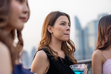 Photo of an elegant beautiful young businesswoman looking thoughtful while holding a blue cocktail in a company celebration event with 2 of her friends or teammates.