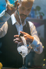 Professional barman in a white shirt and black apron making beautiful cocktail at party in nightclub. Nightlife.