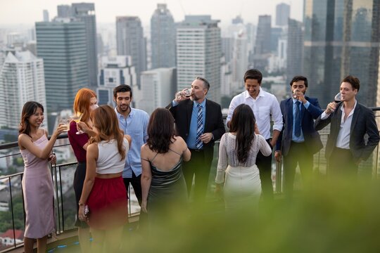 Photo of a group of businessmen and businesswomen mingle with each other drinking wine and champagne on a rooftop bar celebrating the successful of company latest deal and hit target goal of the year