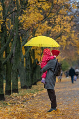 Mother holds small child and large yellow umbrella in her arms. Walk in the autumn park. Vertical frame