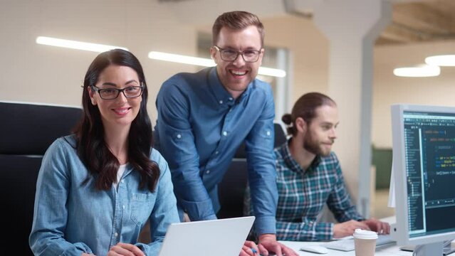 Caucasian cheerful young professional people working in modern office looking at camera and smiling. Male boss speaking with beautiful female and man manager employees at workplace. Portrait
