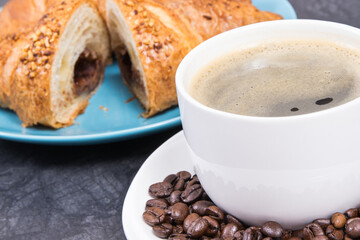 Cup of coffee and fresh croissant with chocolate on plate for breakfast