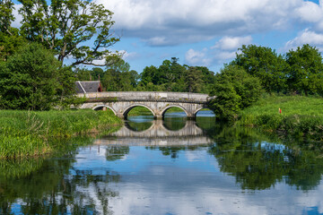 Fototapeta na wymiar old stone bridge reflecting in a still river in green Irish countryside in spring