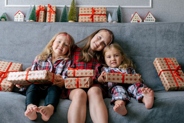 Three little sisters with gift boxes sitting on couch. Happy kids at home portrait.