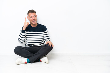 Young man sitting on the floor isolated on white background intending to realizes the solution while lifting a finger up