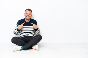Fototapeta premium Young man sitting on the floor isolated on white background with surprise facial expression
