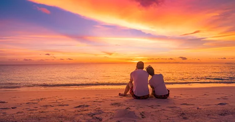 Zelfklevend Fotobehang Love couple watching sunset together on beach travel summer holidays. People silhouette from behind sitting enjoying view sunset sea tropical island, destination vacation. Romantic freedom lifestyle © icemanphotos
