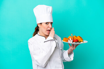 Young caucasian chef woman holding waffles isolated on blue background whispering something