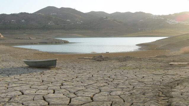 Cracked land by drought with a small boat in the shore of a pond
