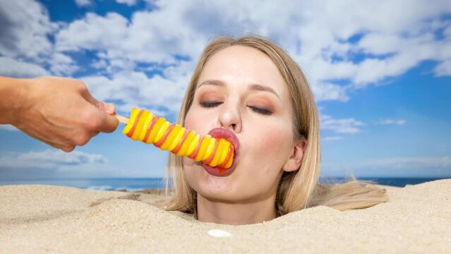 Woman buried in sand on beach licking a lolly