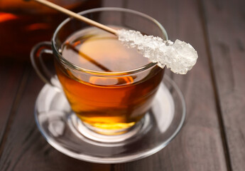 Stick with sugar crystals and cup of tea on wooden table, closeup