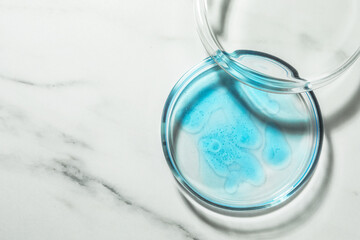 Petri dish with liquid and lid on white marble table, flat lay. Space for text