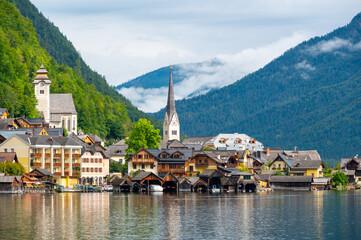 Fototapeta na wymiar Hallstatt Village and Hallstatter See lake in Austria. Scenery with famous old church near the lake. Clouds and mist over the mountains in background. Famous tourist destination.