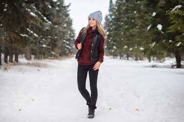 portrait of a happy girl in a blue hat, sweater and vest, stands on a snowy winter alley