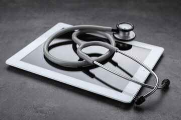 Computer tablet with stethoscope on grey table, closeup