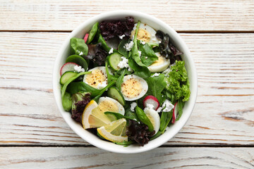 Delicious salad with boiled eggs, vegetables and lemon in bowl on white wooden table, top view